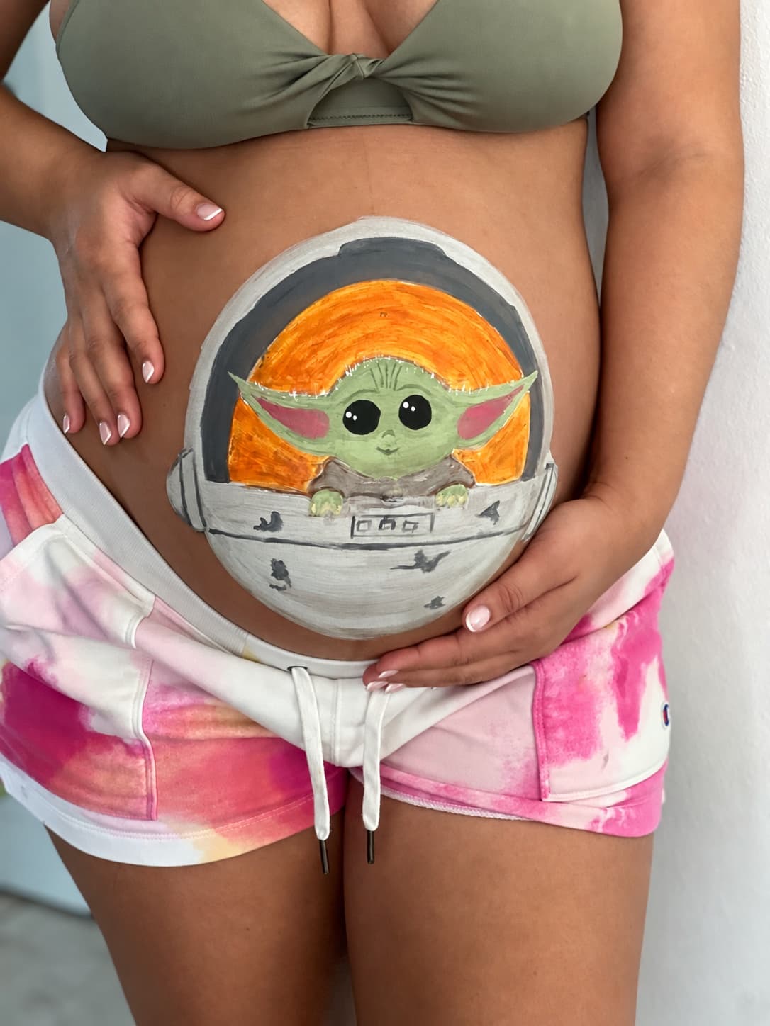 A green space character in a silver pod painted on an expectant parent's belly